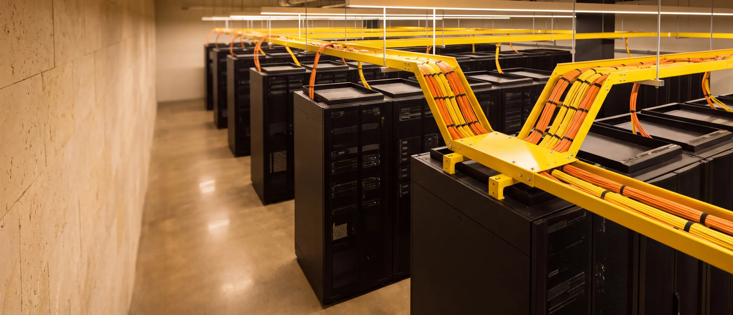 A yellow overhead fibre raceway branching into separate routes above rows of black equipment racks