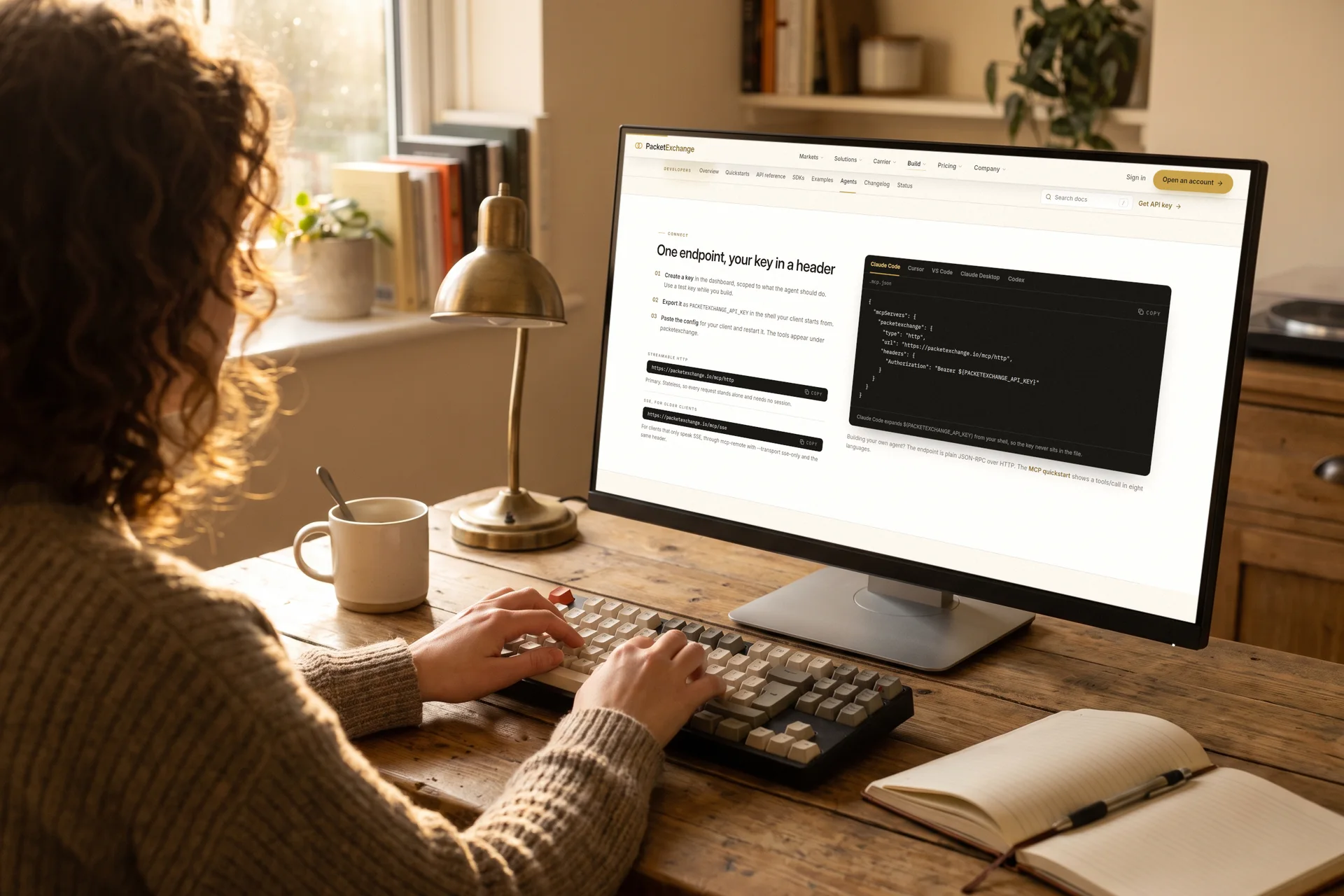 A developer at a desk with a monitor open at the PacketExchange agents page, showing the Claude Code MCP configuration