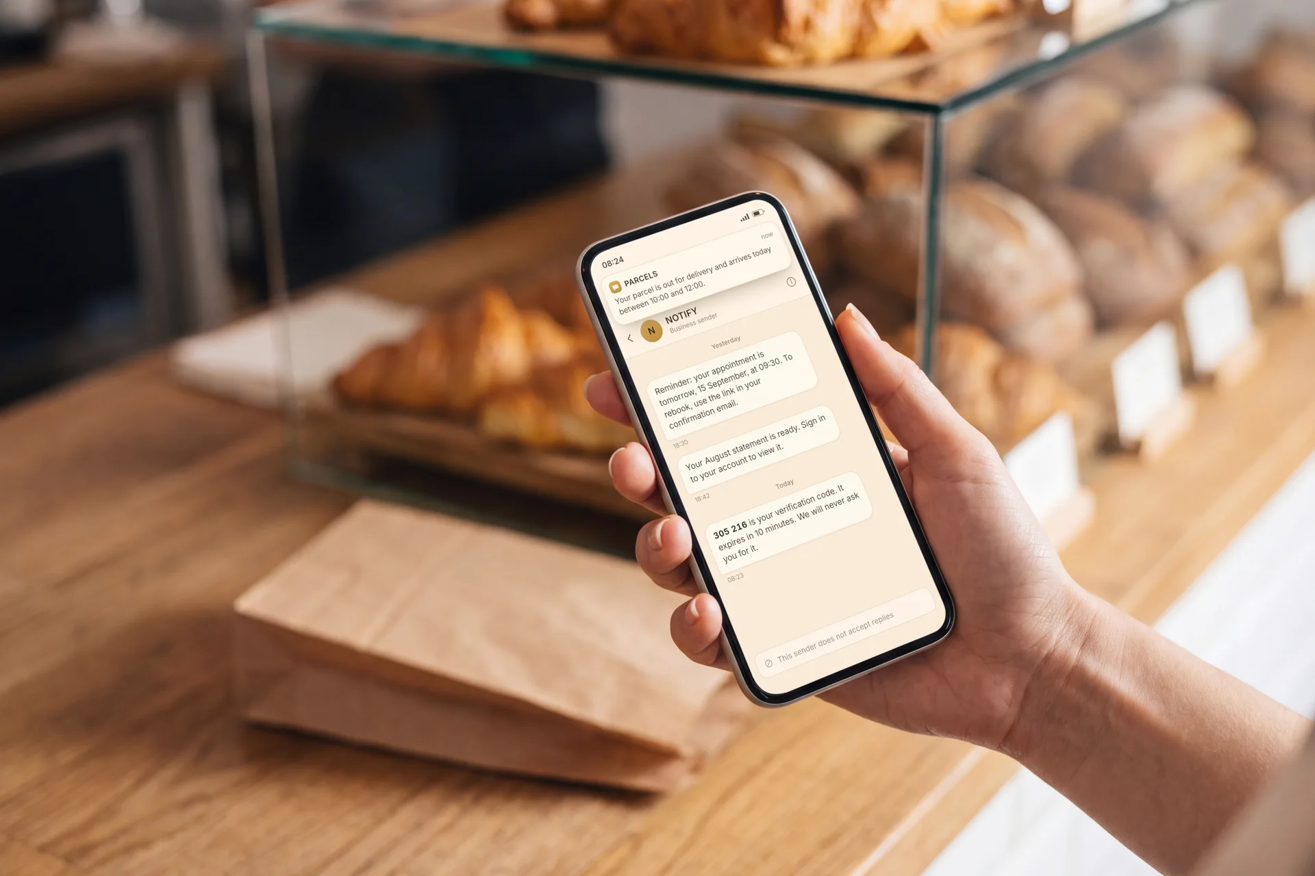A hand at a bakery counter holding a phone that shows a thread of business text messages
